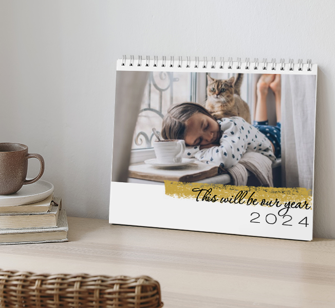 A calendar propped on a wooden table with a photo of two women hugging in the water with the text on the front 'Wanderlust Adventure Awaits, Go Find It'