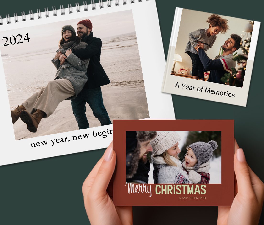 Closed calendar with photo of couple on the beach during winter that reads 'new year, new beginnings 2024', closed premium mini book with photo of dad and daughter decorating a christmas tree that reads 'A Year of Memories' and hands holding a greeting card showing a family outside during winter that reads 'Merry Christmas'.