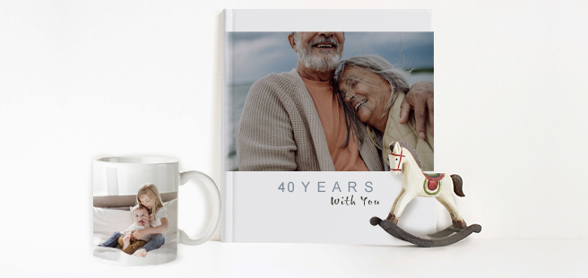 Closed photobook showing photo of older couple on front that reads '40 years with you' and a white mug showing a photo of young brother and sister.